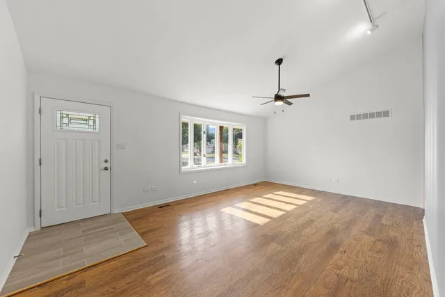 an empty room with wooden floor chandelier and windows