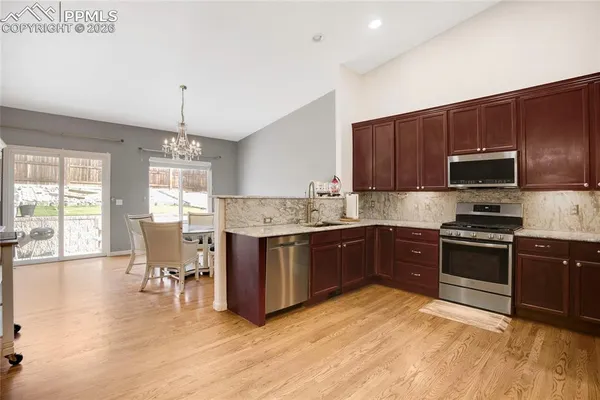 a kitchen with stainless steel appliances granite countertop a stove top oven a sink dishwasher a dining table and chairs with wooden floor