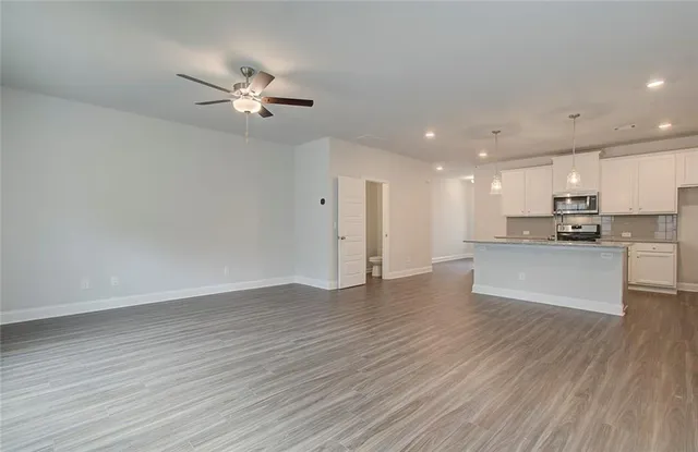 a view of an empty room with kitchen appliances and a ceiling fan