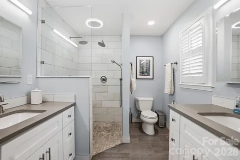 a bathroom with a granite countertop sink a toilet a shower and a window
