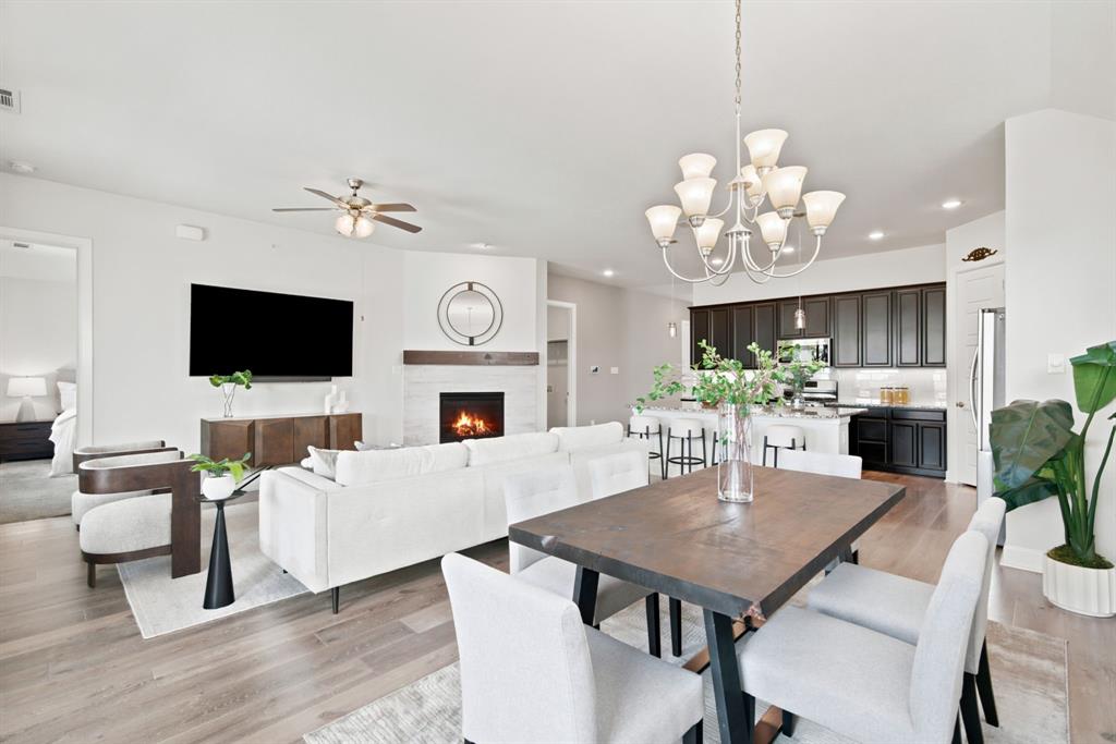 709 Bent Brook Road Oak Point, TX 75068 - Photo 1 of 27 Open-concept living area featuring wood-finish flooring, a contemporary chandelier, a corner fireplace with a white tile surround and wood mantel, and a ceiling fan