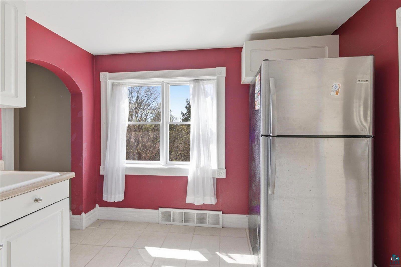 50 Main Street Soudan, MN 55782 - Photo 3 of 31 Kitchen area featuring a stainless steel refrigerator, white cabinetry, a built-in sink, tiled flooring, and an arched doorway