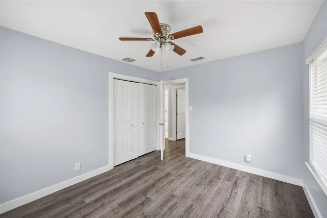 an empty room with wooden floor ceiling fan and windows