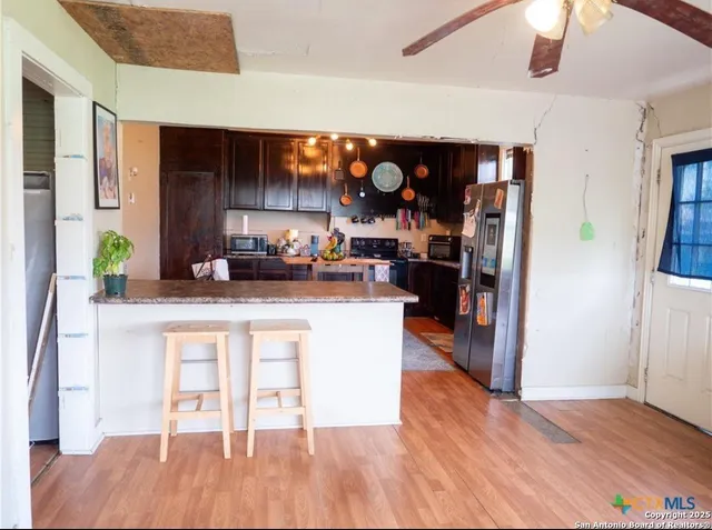 a living room with stainless steel appliances kitchen island granite countertop a refrigerator a stove and a wooden floors