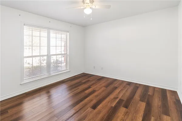an empty room with wooden floor chandelier fan and windows