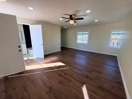 a view of an empty room with wooden floor and a ceiling fan