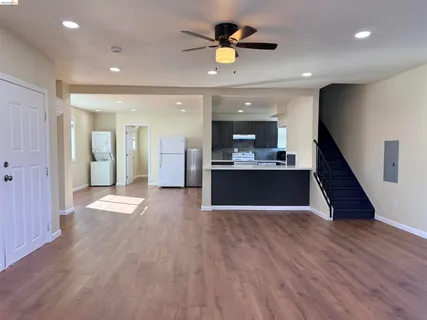 a view of empty room with wooden floor and kitchen view