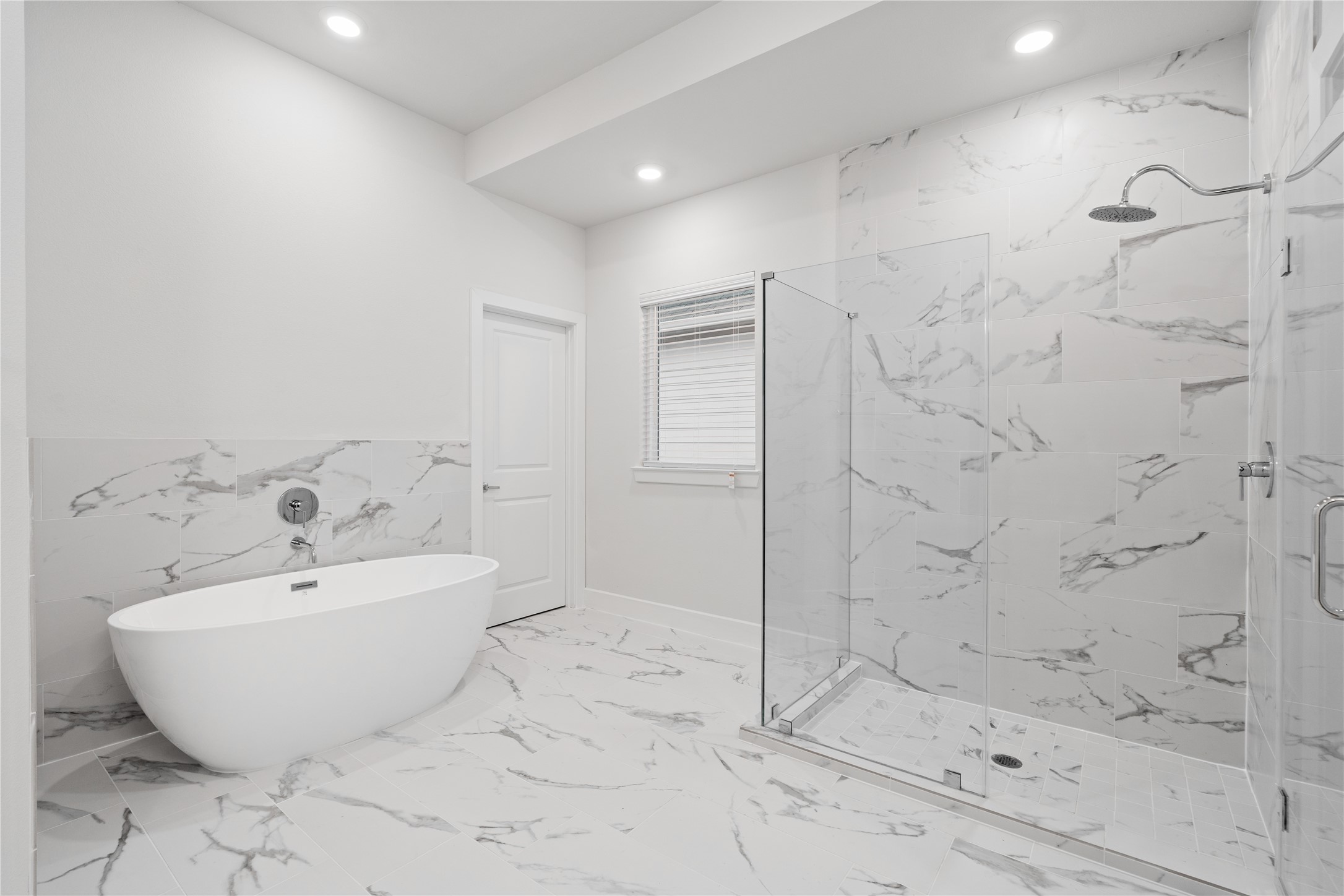 6451 Rena Street Houston, TX 77092 - Photo 24 of 33 Freestanding soaking tub positioned across from a glass enclosed shower wrapped in large format tile, creating a layout that feels open rather than compressed.