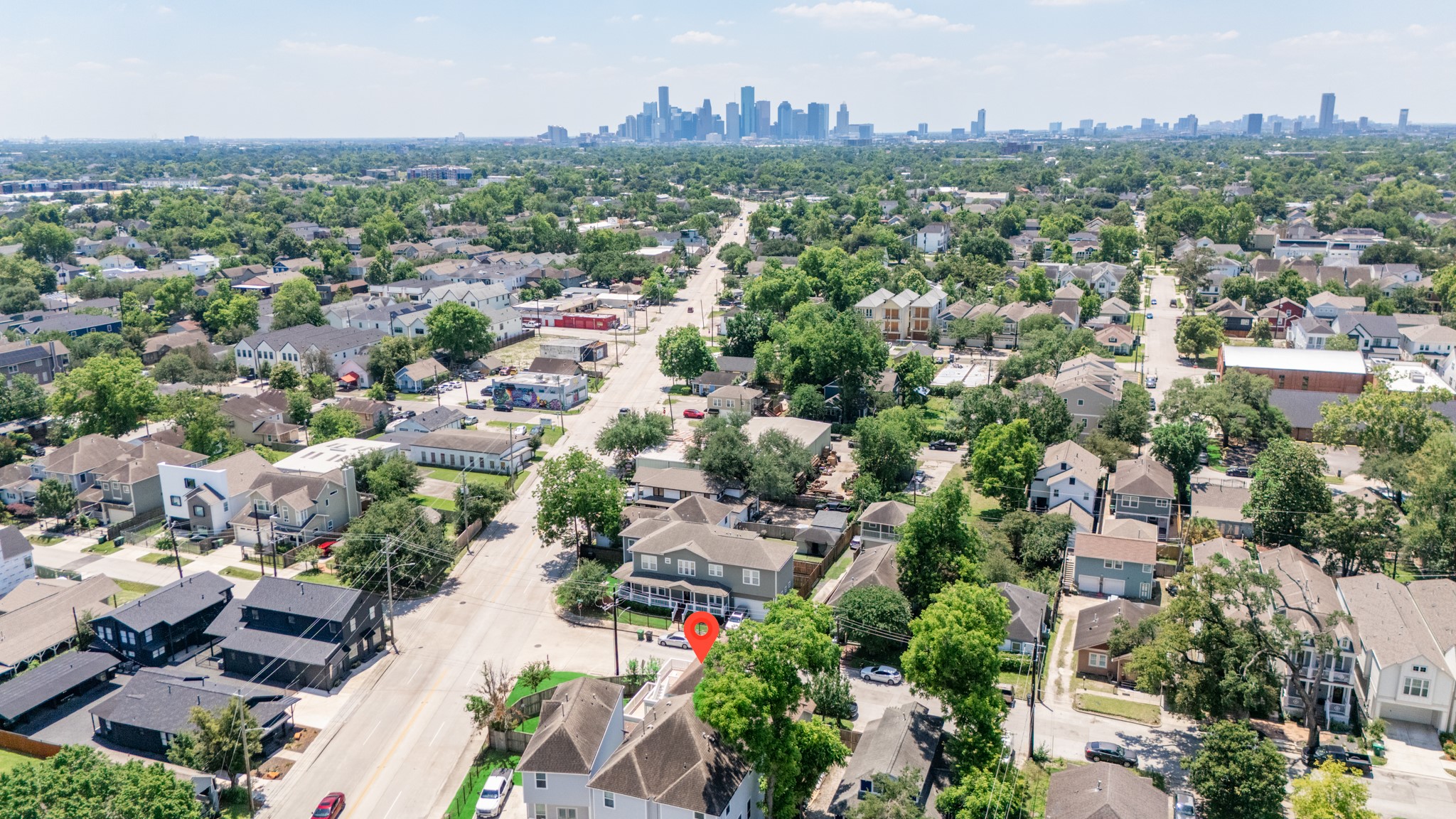 6621 North Main Street Houston, TX 77009 - Photo 37 of 41 Aerial view of a suburban neighborhood with tree-lined streets and a mix of modern and traditional homes. The city skyline is visible in the distance, indicating urban proximity. The area appears vibrant and well-connected, offering a blend of residential charm and city convenience.