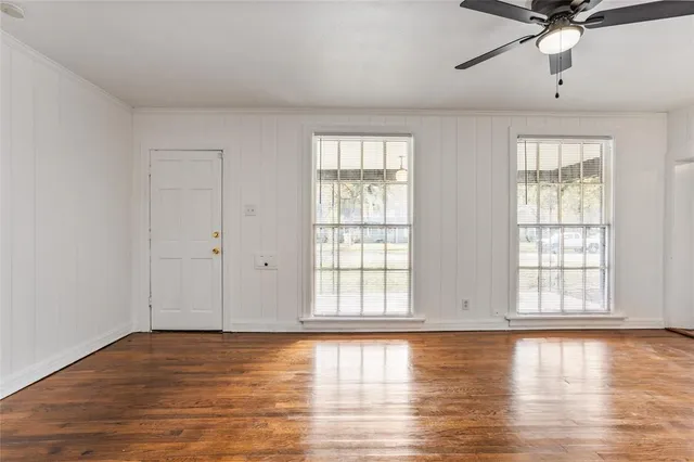 an empty room with wooden floor fan and windows