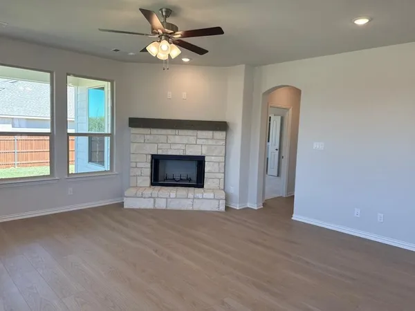 an empty room with windows fireplace and a ceiling fan