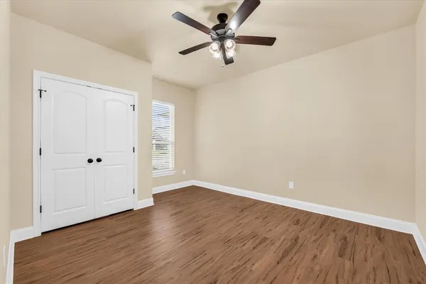 an empty room with wooden floor ceiling fan and window
