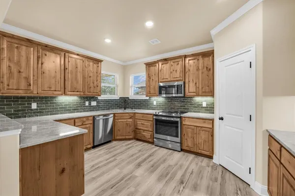 a kitchen with stainless steel appliances granite countertop wooden cabinets a stove a sink and dishwasher with wooden floor
