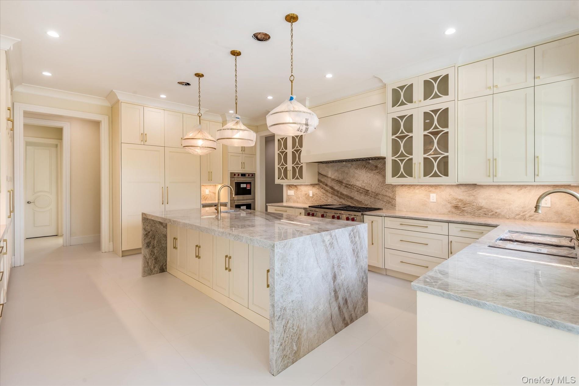 566 A East Shore Road Queens, NY 11024 - Photo 13 of 42 Kitchen featuring glass insert cabinets, light stone countertops, decorative backsplash, decorative light fixtures, and a kitchen island with sink