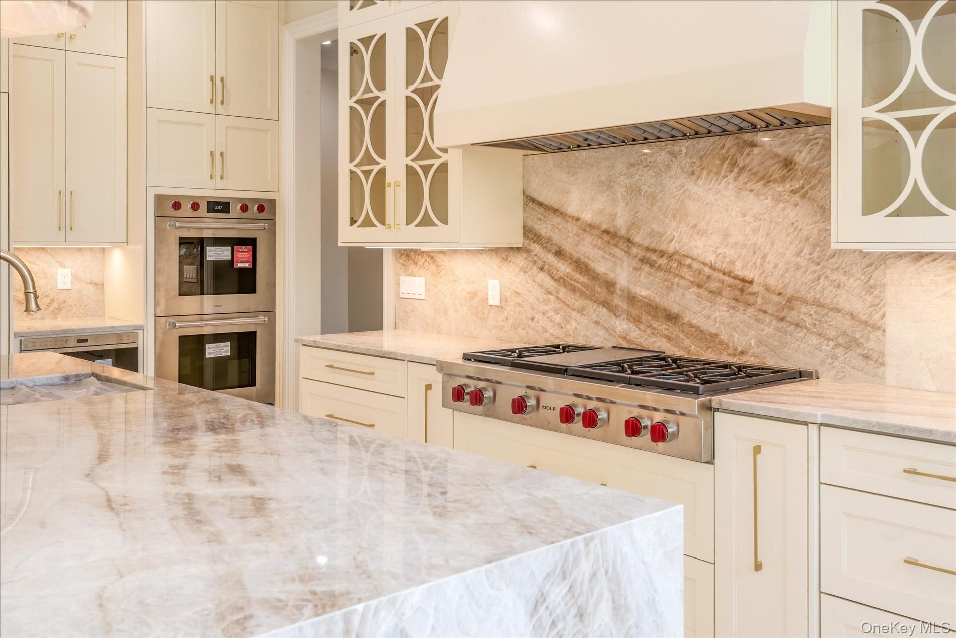 566 A East Shore Road Queens, NY 11024 - Photo 14 of 42 Kitchen with light stone counters, glass insert cabinets, custom range hood, and tasteful backsplash