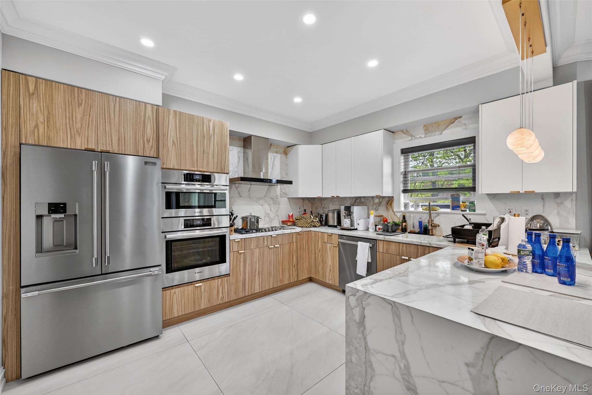 65 Wildway Bronxville, NY 10708 - Photo 35 of 42 Contemporary kitchen featuring wood-finish and white cabinetry, stainless steel appliances including a built-in oven and microwave, a gas range with a range hood, and a waterfall-edge island with a marble-style surface