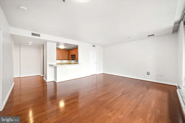 an empty room with wooden floor and a kitchen space