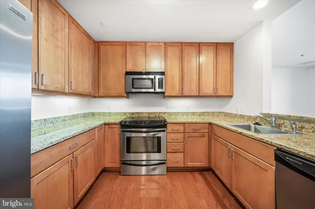 a kitchen with stainless steel appliances granite countertop wooden cabinets a sink and dishwasher a stove with wooden floor