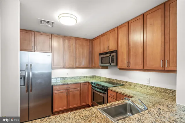 a kitchen with stainless steel appliances granite countertop a refrigerator a stove and a sink with wooden cabinets
