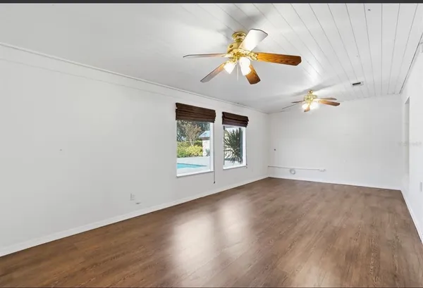 an empty room with wooden floor chandelier fan and windows