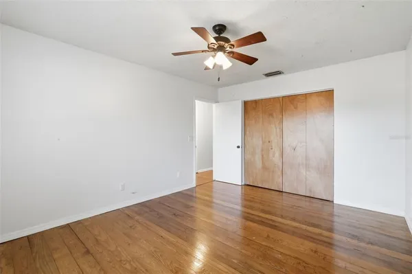 an empty room with wooden floor fan and windows