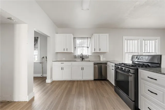 a kitchen with a hard wood floor white cabinets and stainless steel appliances