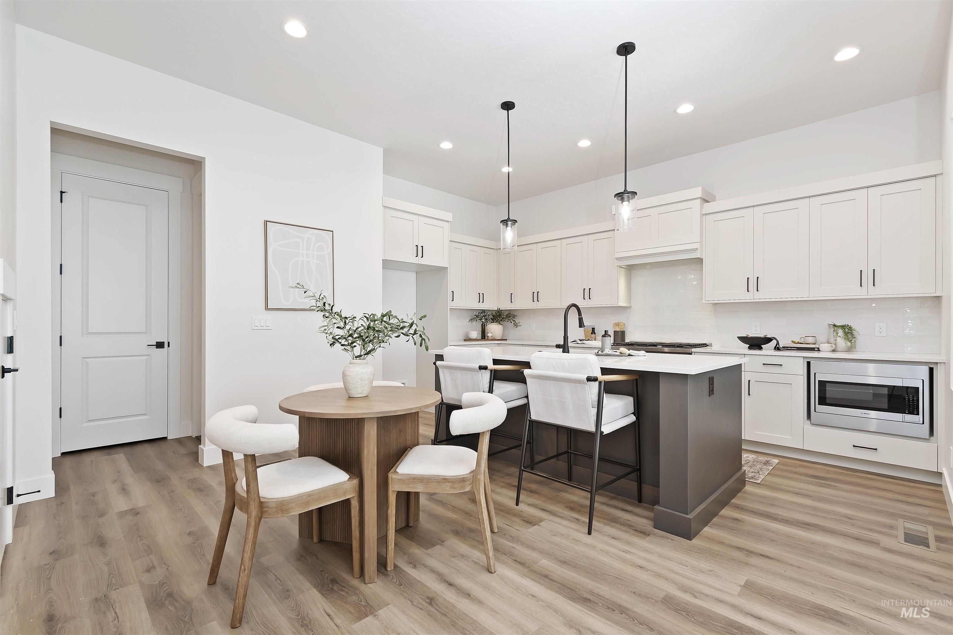 724 South Calhoun Lane Star, ID 83669 - Photo 12 of 46 Kitchen with backsplash, white cabinetry, hanging light fixtures, an island with sink, and light wood-style floors