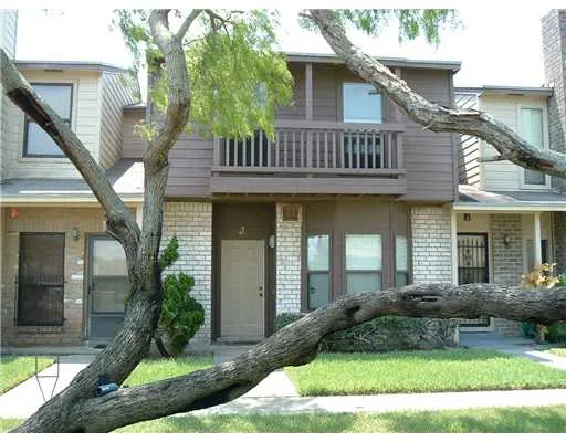 a view of a house with brick walls plants and large tree