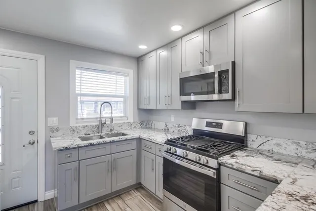 a kitchen with stainless steel appliances granite countertop a refrigerator a sink dishwasher a stove and white cabinets with wooden floor