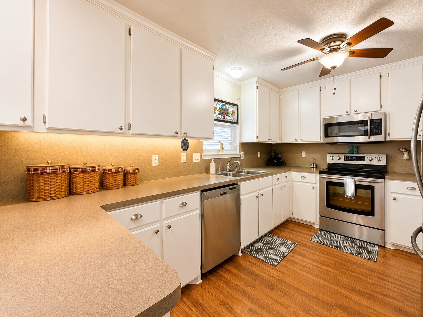 135 Sand Shoals Road Freeport, TX 77541 - Photo 8 of 20 This kitchen features a modern, inviting design with white cabinetry, stainless steel appliances, and warm wood flooring. It includes ample counter space, a ceiling fan, and under-cabinet lighting for a bright and functional cooking area.