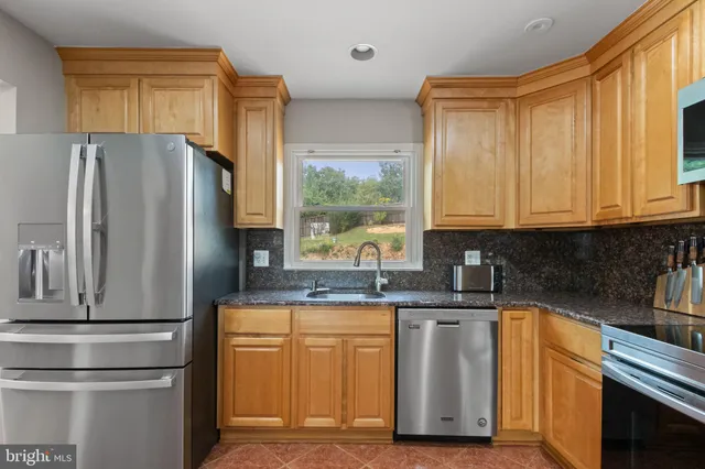 a kitchen with stainless steel appliances granite countertop a refrigerator a stove top oven a sink dishwasher and white cabinets with wooden floor