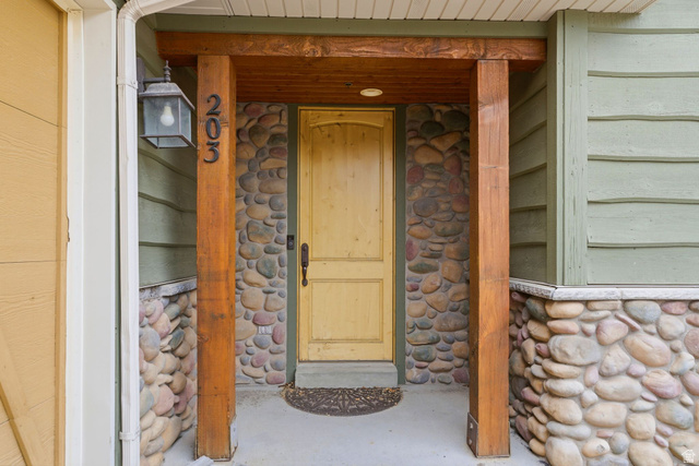3634 North Huntsman Path, Unit C203 Eden, UT 84310 - Photo 21 of 27 Entryway featuring a natural wood door, stacked stone facade, exposed wood beams, and a concrete porch
