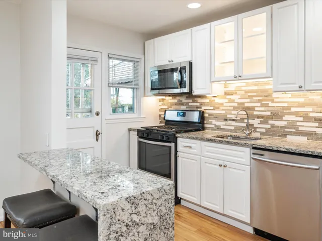 a kitchen with stainless steel appliances kitchen island granite countertop a sink dishwasher stove and white cabinets with wooden floor