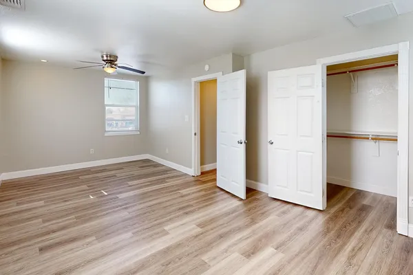 an empty room with wooden floor a ceiling fan and windows