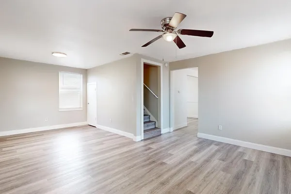 an empty room with wooden floor chandelier fan and windows