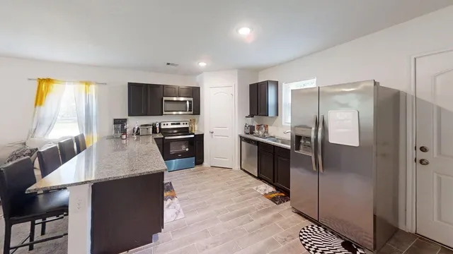 a kitchen with stainless steel appliances granite countertop a refrigerator a stove a sink a dining table and chairs