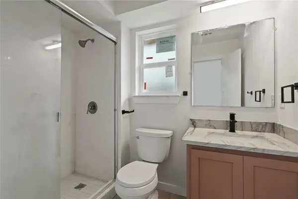 a bathroom with a granite countertop toilet a sink a mirror and shower
