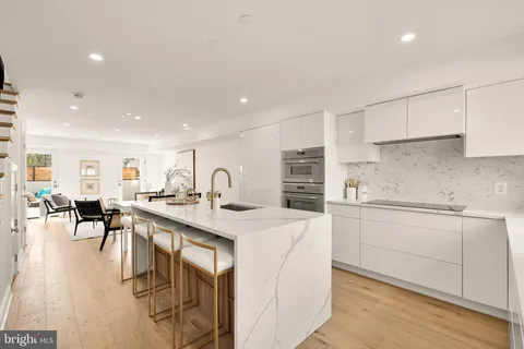 a kitchen with white cabinets a sink stove and chairs with wooden floor