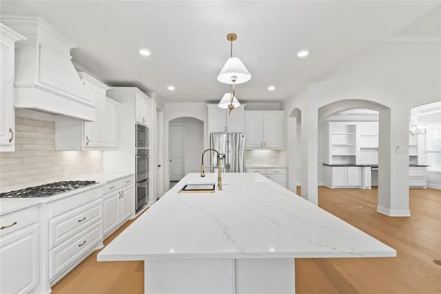 a large white kitchen with wooden floor and stainless steel appliances