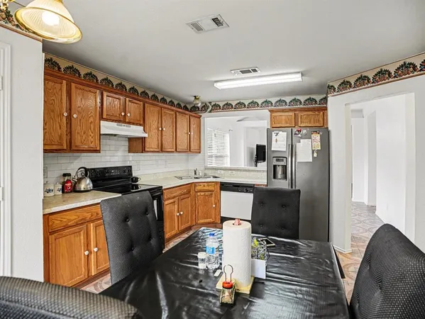 a kitchen with stainless steel appliances granite countertop a refrigerator a sink dishwasher a stove and a dining table with wooden floor