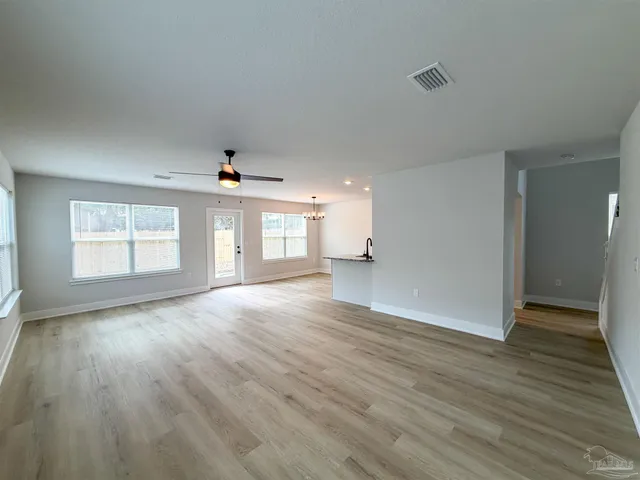 an empty room with wooden floor chandelier and windows