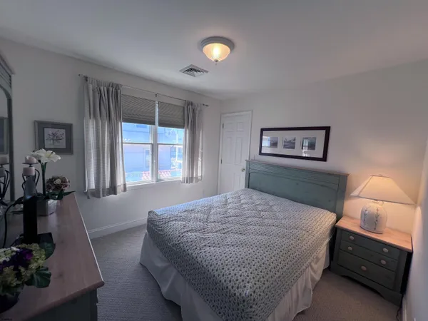 a bedroom with a bed and a lamp on dresser with a window