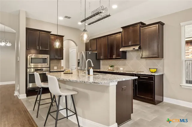 a kitchen with stainless steel appliances granite countertop a sink a stove a refrigerator cabinets and chairs