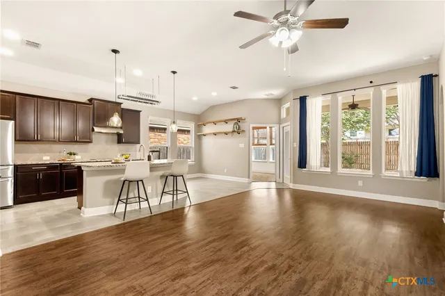 a kitchen with stainless steel appliances granite countertop a stove top oven a refrigerator a sink and a dining table with wooden floors