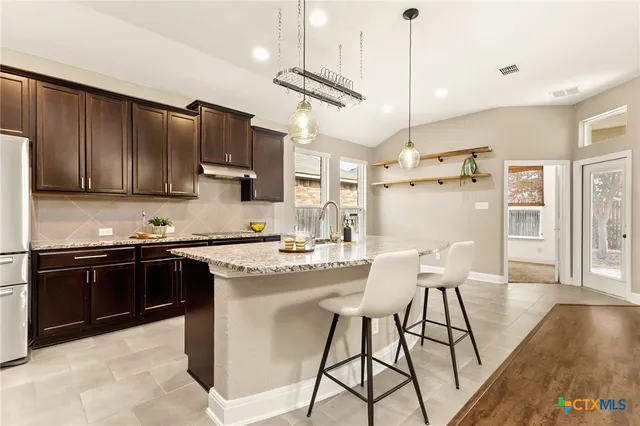 a kitchen with stainless steel appliances granite countertop a stove top oven a refrigerator a sink and chairs