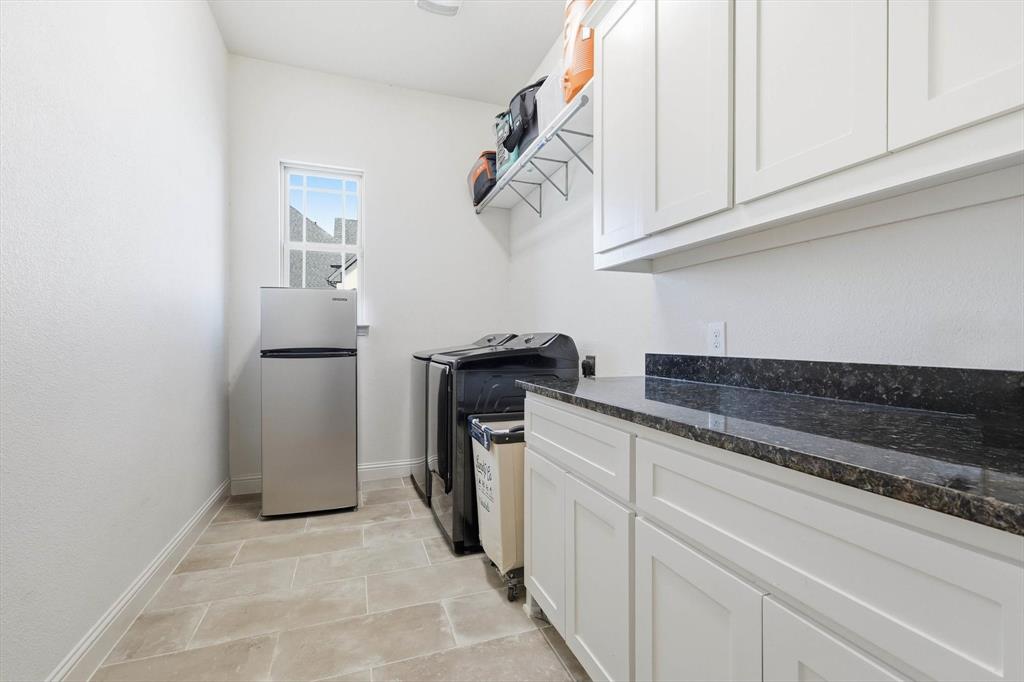 7751 Faught Road Northlake, TX 76226 - Photo 27 of 39 Laundry room featuring tile flooring, white cabinetry, dark stone countertops, and a window providing natural light