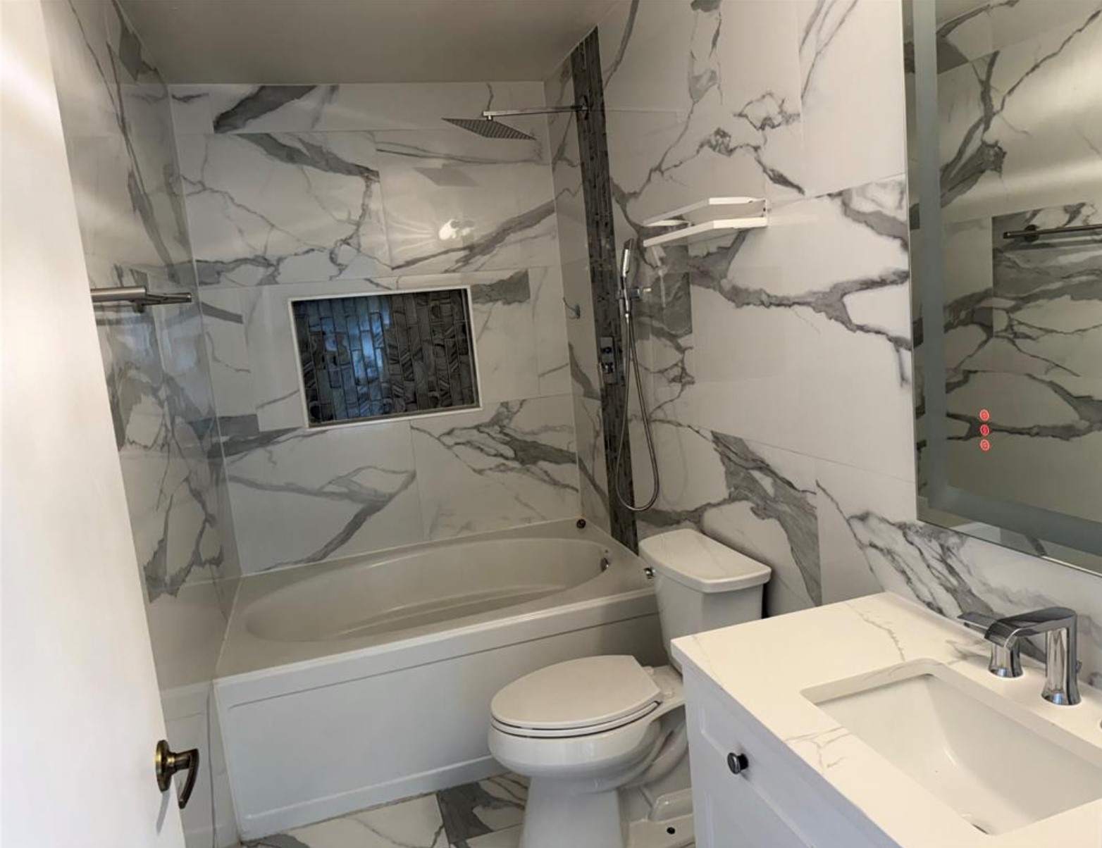 6600 Glebe Path Austin, TX 78754 - Photo 9 of 11 Elegant white marble-patterned tile envelops this contemporary bathroom, featuring a deep soaking tub and a sleek vanity.