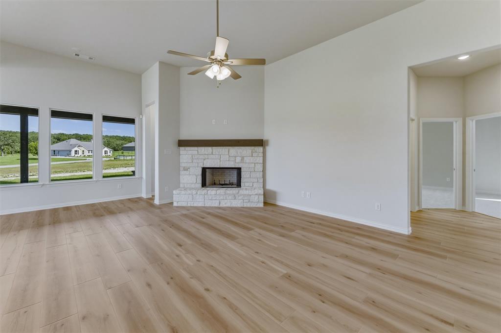605 Tay Tay Way Springtown, TX 76082 - Photo 13 of 31 Spacious living area featuring wood-finish flooring, a stone fireplace with a wood mantel, and multiple large windows