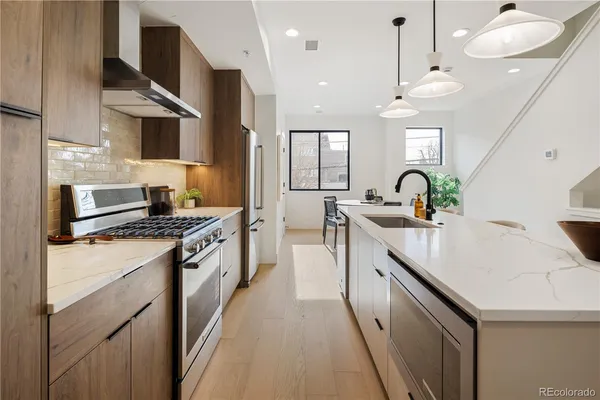 a kitchen with stainless steel appliances kitchen island a refrigerator a stove a sink a dining table and chairs with wooden floor