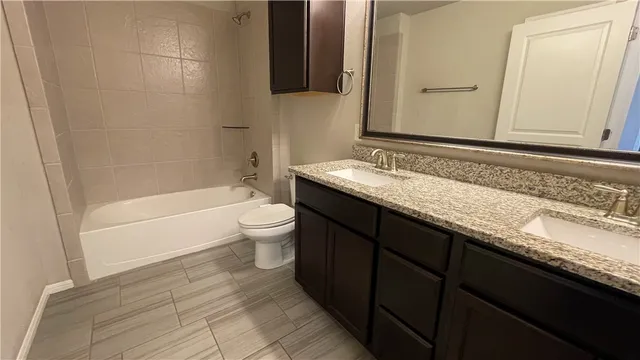 a bathroom with a granite countertop bathtub sink vanity mirror and toilet